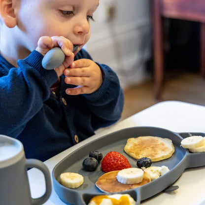 Toddler using silicone cutlery set, enjoying pancakes and fruit on a toddler-friendly plate, perfect for self-feeding.