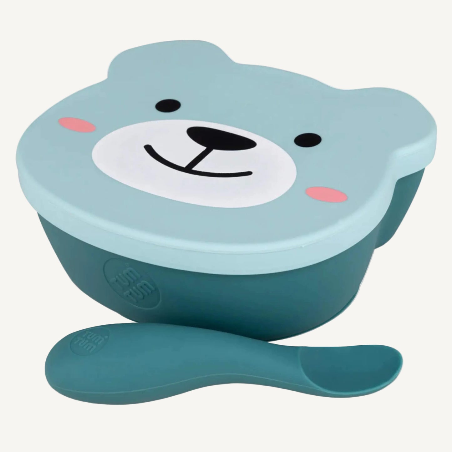 A close-up view of a suction weaning bowl with a fitted lid and a soft weaning spoon placed in front, showing the rounded bowl shape and easy-grip spoon design.