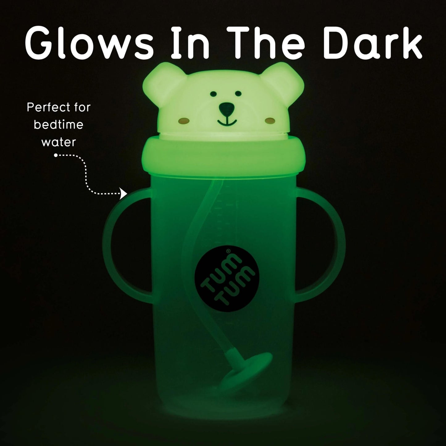 A glow-in-the-dark sippy cup with a bear-shaped lid, shown glowing green in the dark. The cup has two side handles, a straw, and a black circular logo that reads 'tum tum'.