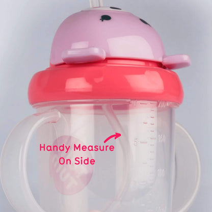 Close-up of a clear sippy cup with moulded volume markings, shown with on-image text reading “Handy Measure On Side,” and a pink screw-on lid with an internal straw visible.
