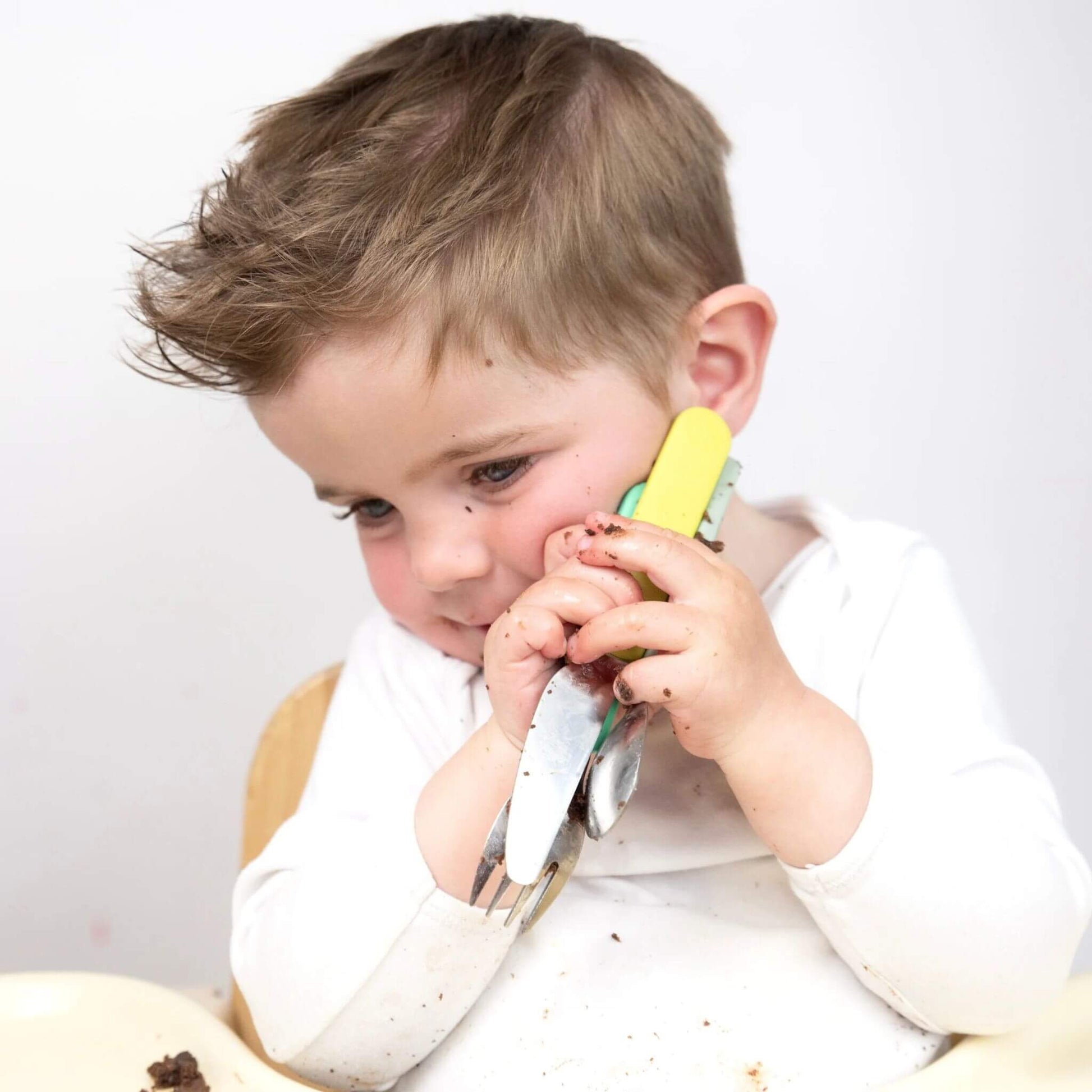 A toddler holding a cutlery set, featuring Stanley Sloth handles on the fork and spoon. The set is designed for easy grip and self-feeding.