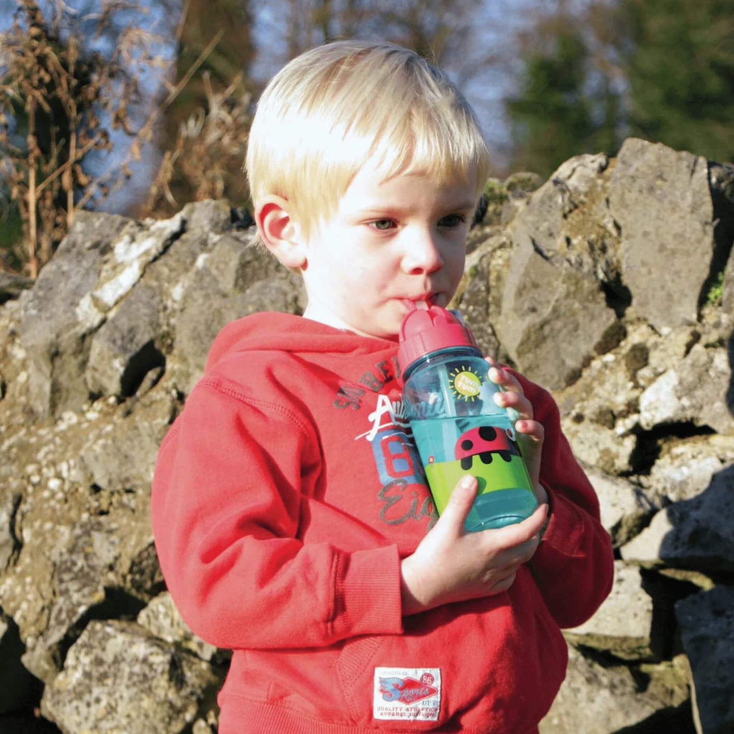 Child drinking from brightly illustrated water bottle with bugs design, featuring a flip top lid and straw, perfect for keeping kids hydrated.