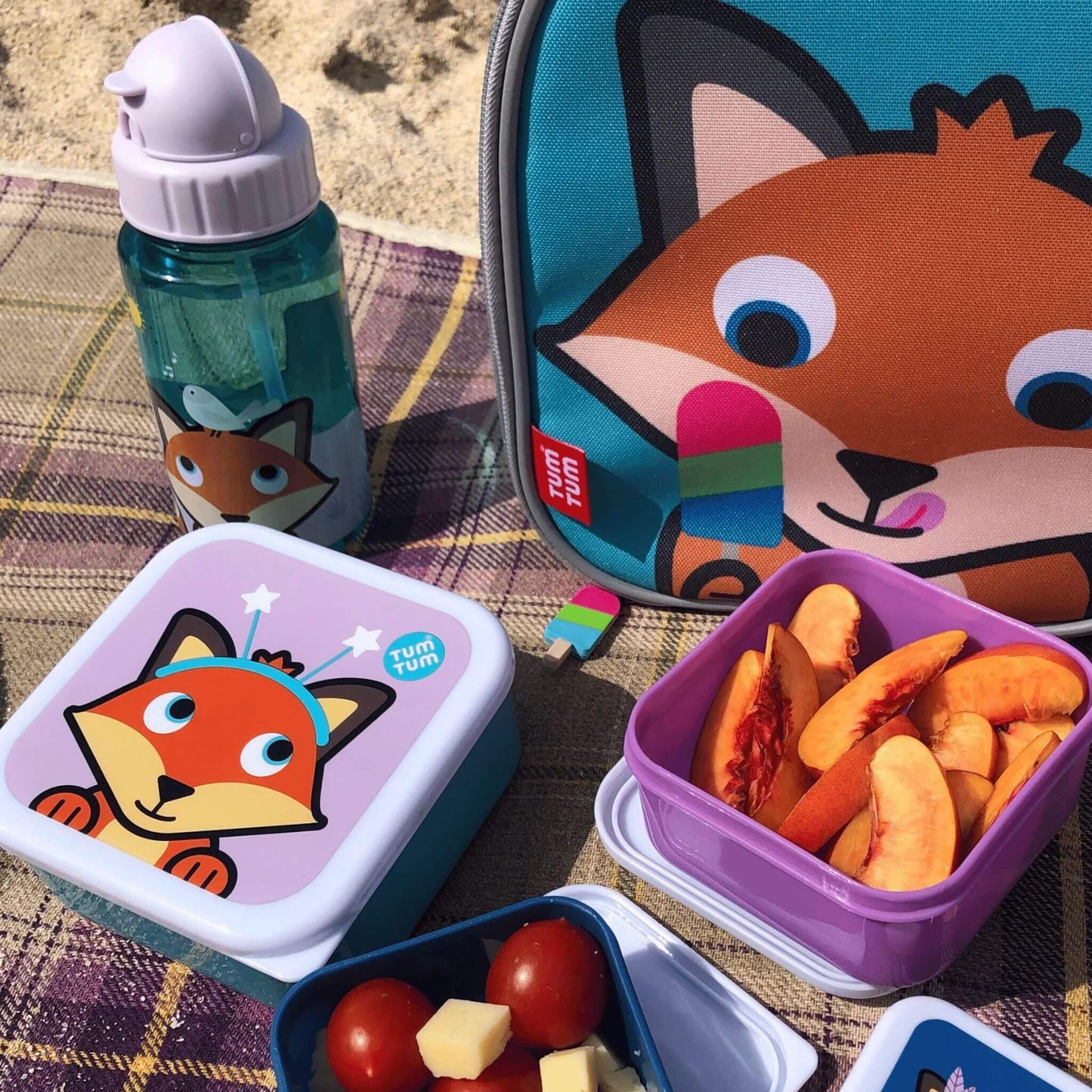 Kid's water bottle with Felicity Fox character design, alongside matching snack boxes and lunch bag, placed on a blanket at the beach, perfect for toddler meals.
