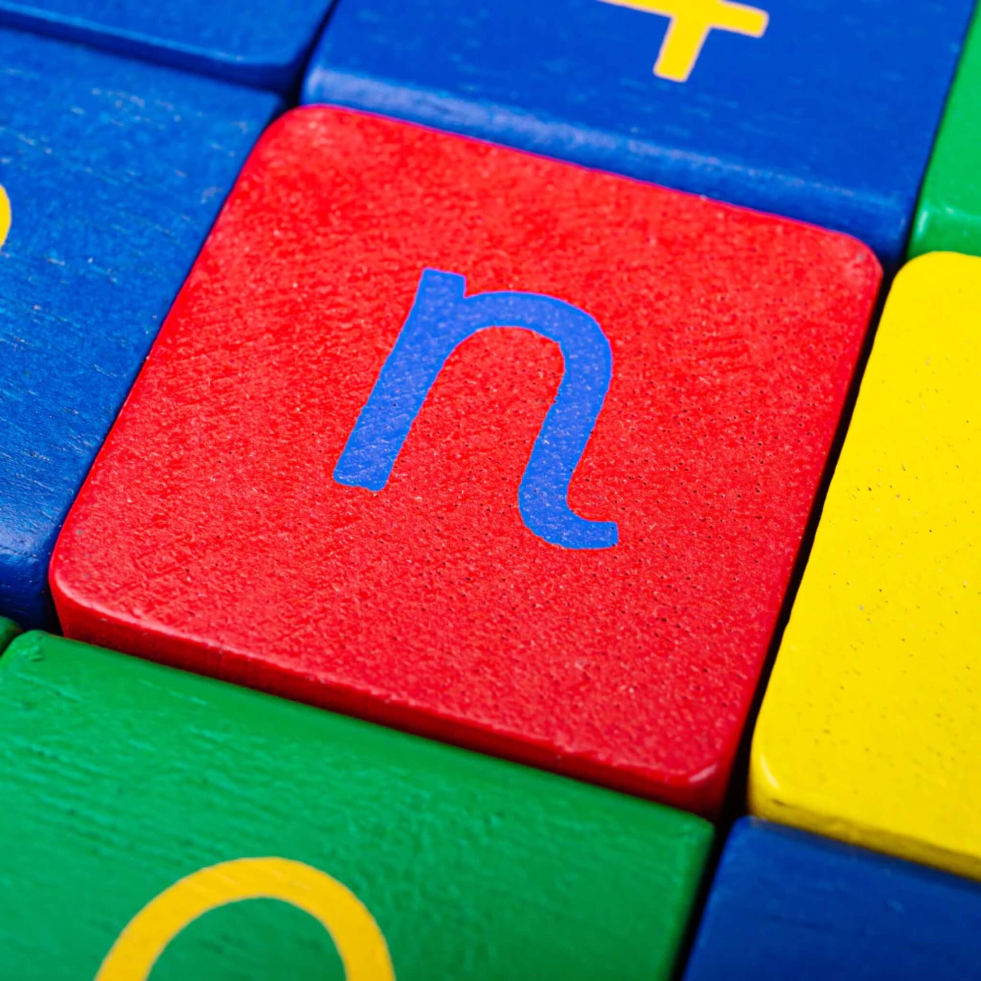 Macro close-up of a red block showing the lowercase blue letter “n” with green, blue and yellow blocks surrounding it.