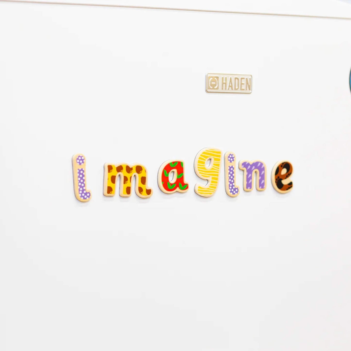 Colourful magnetic letters spelling the word 'Imagine' on a white fridge door with a brand logo.