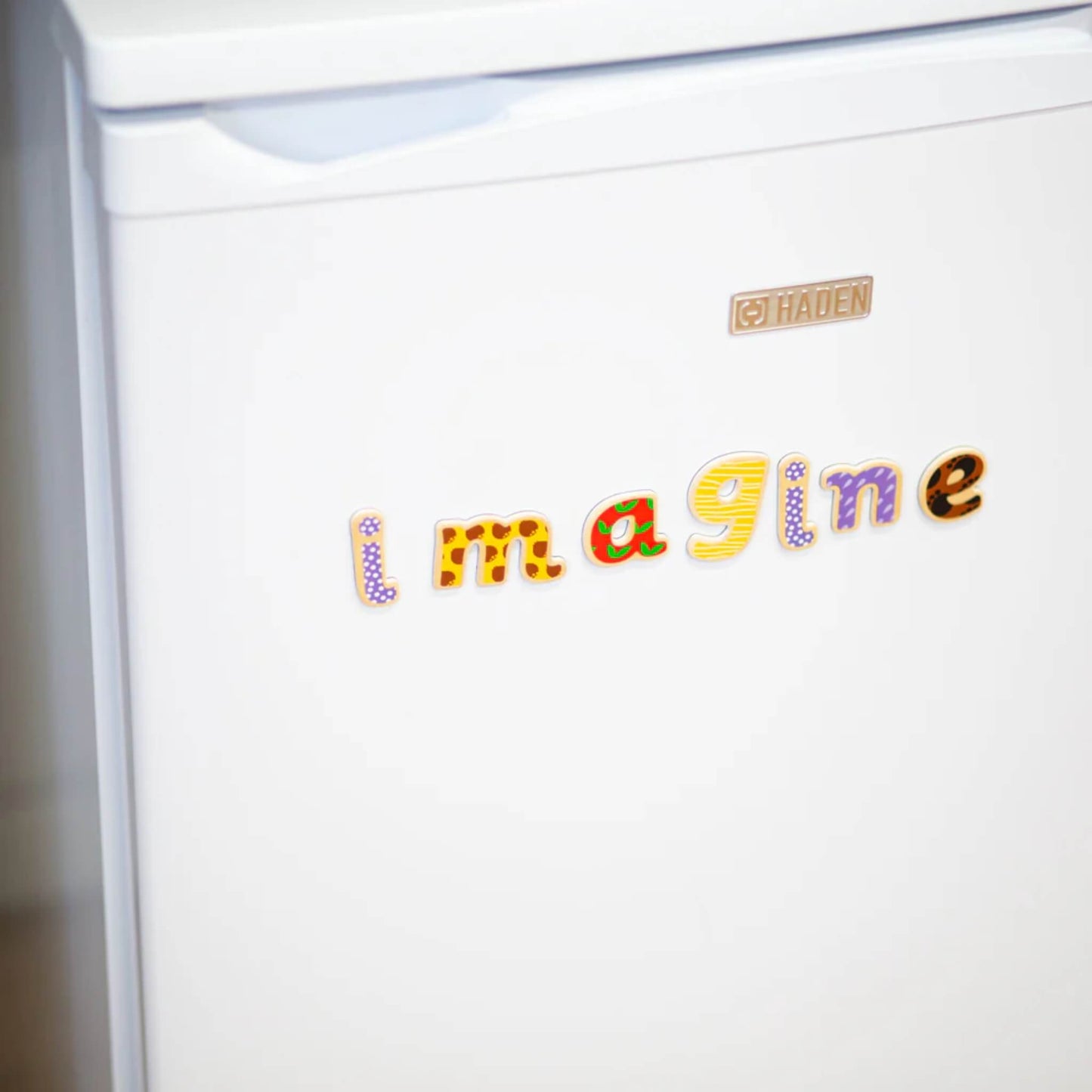 White refrigerator with colorful wooden letters spelling 'Imagine' on the door.