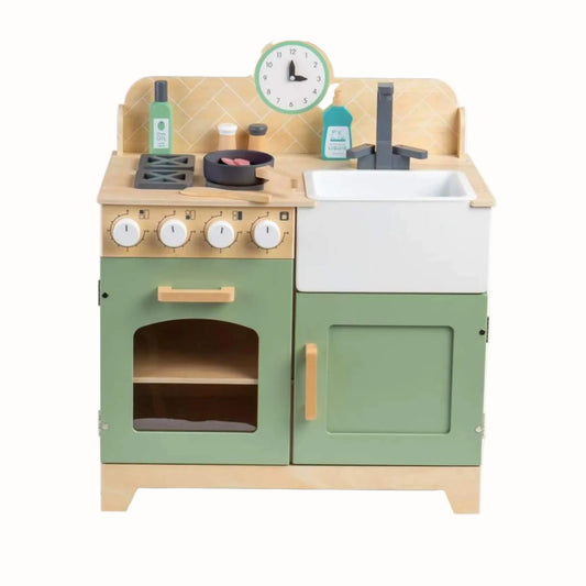 Front view of a green wooden play kitchen with oven, Belfast sink, hob, clock, frying pan and kitchen accessories.