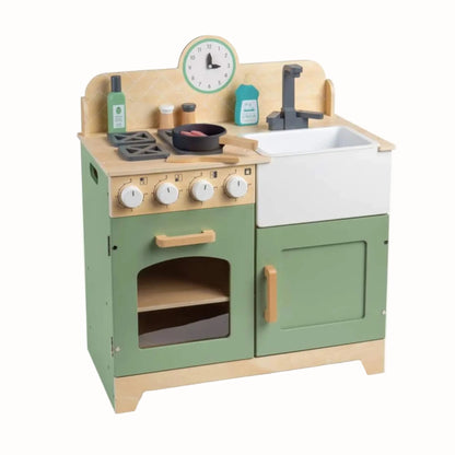 A children's wooden play kitchen set with sage green and natural wood panels, a white sink, toy stove, small bottles, and a round wall clock.