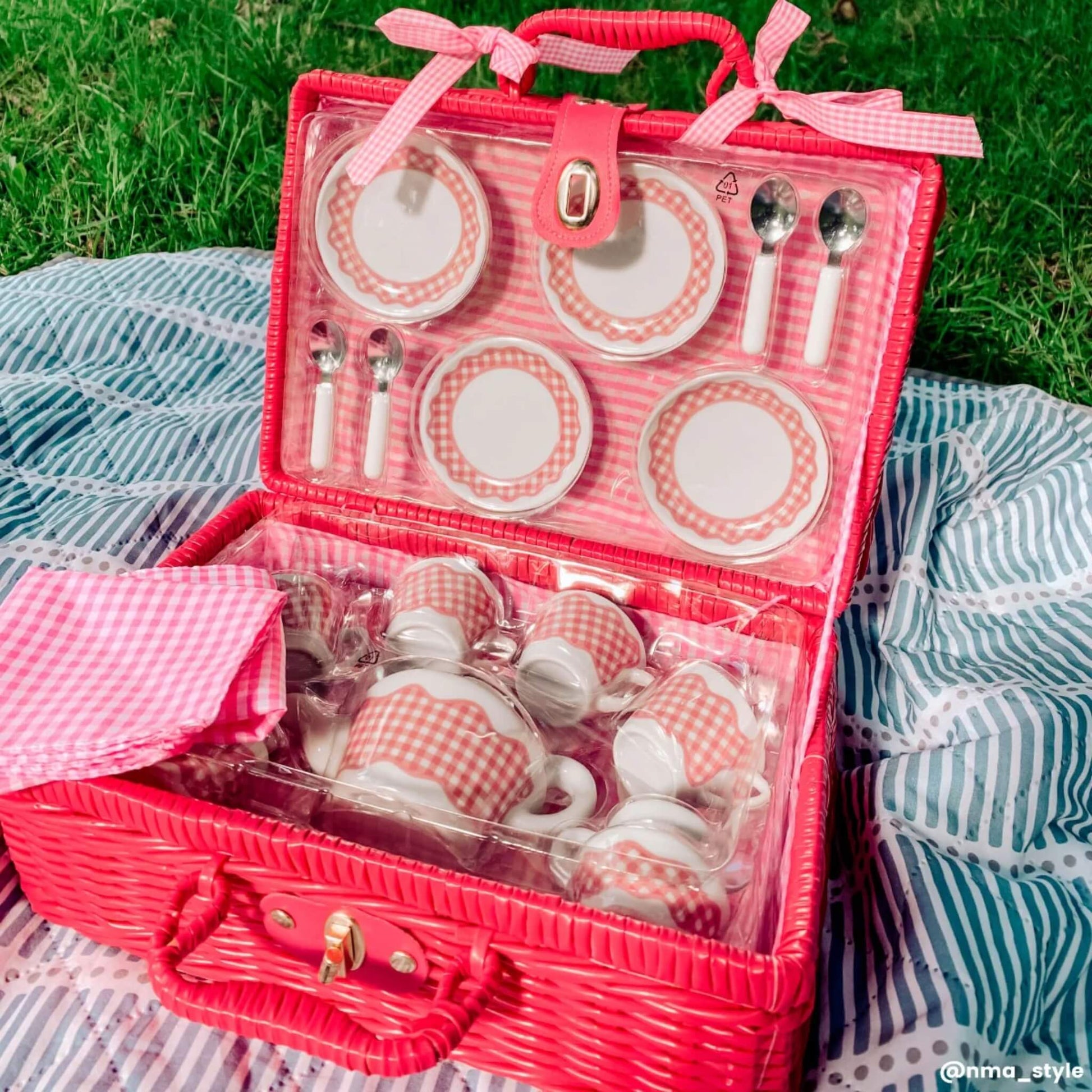 Open Picnic tea set basket placed on a picnic blanket outdoors, with sunlight highlighting the pink gingham porcelain pieces and soft napkins.