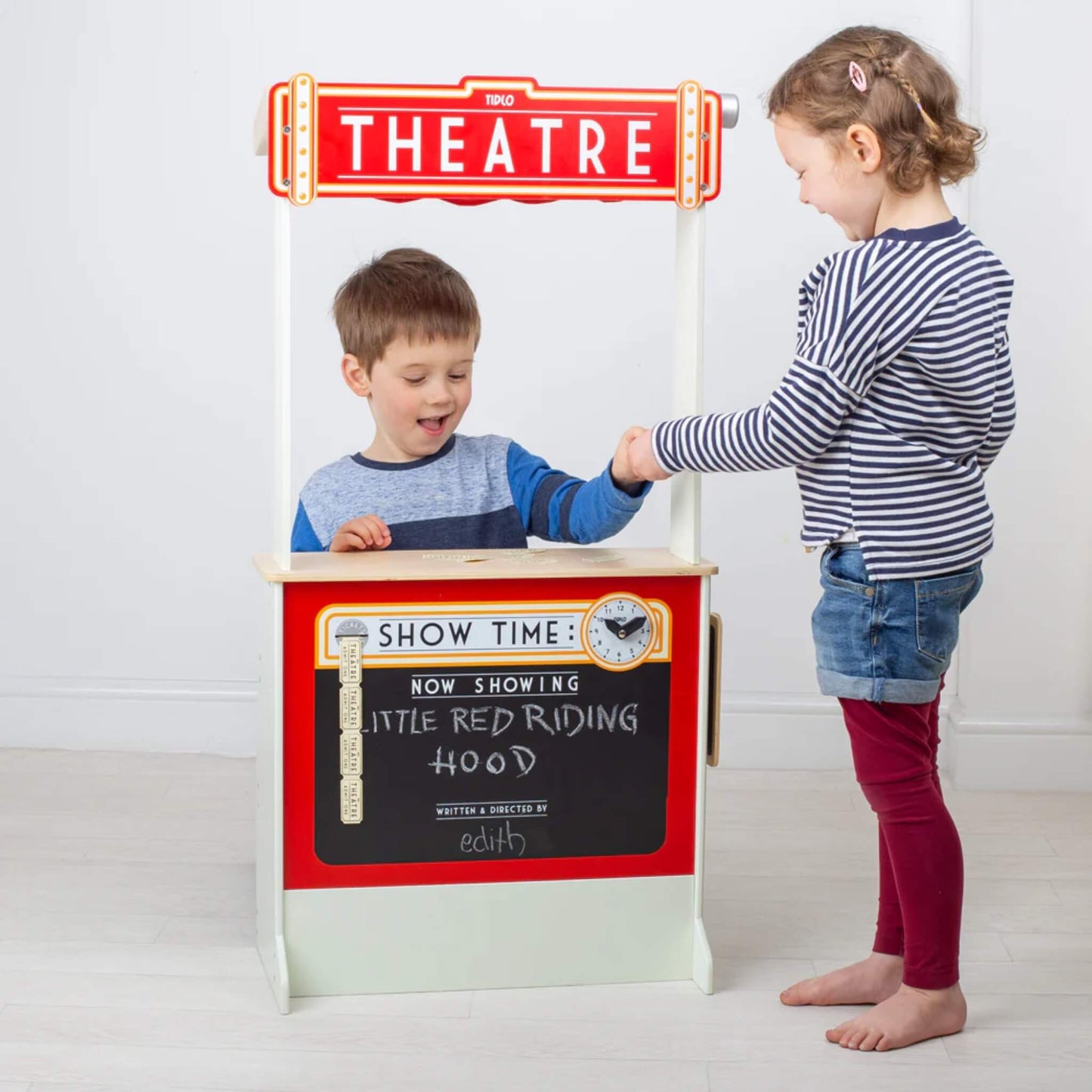 Two children role-playing with the theatre, one behind the stand performing while the other watches, exchanging pretend tickets.