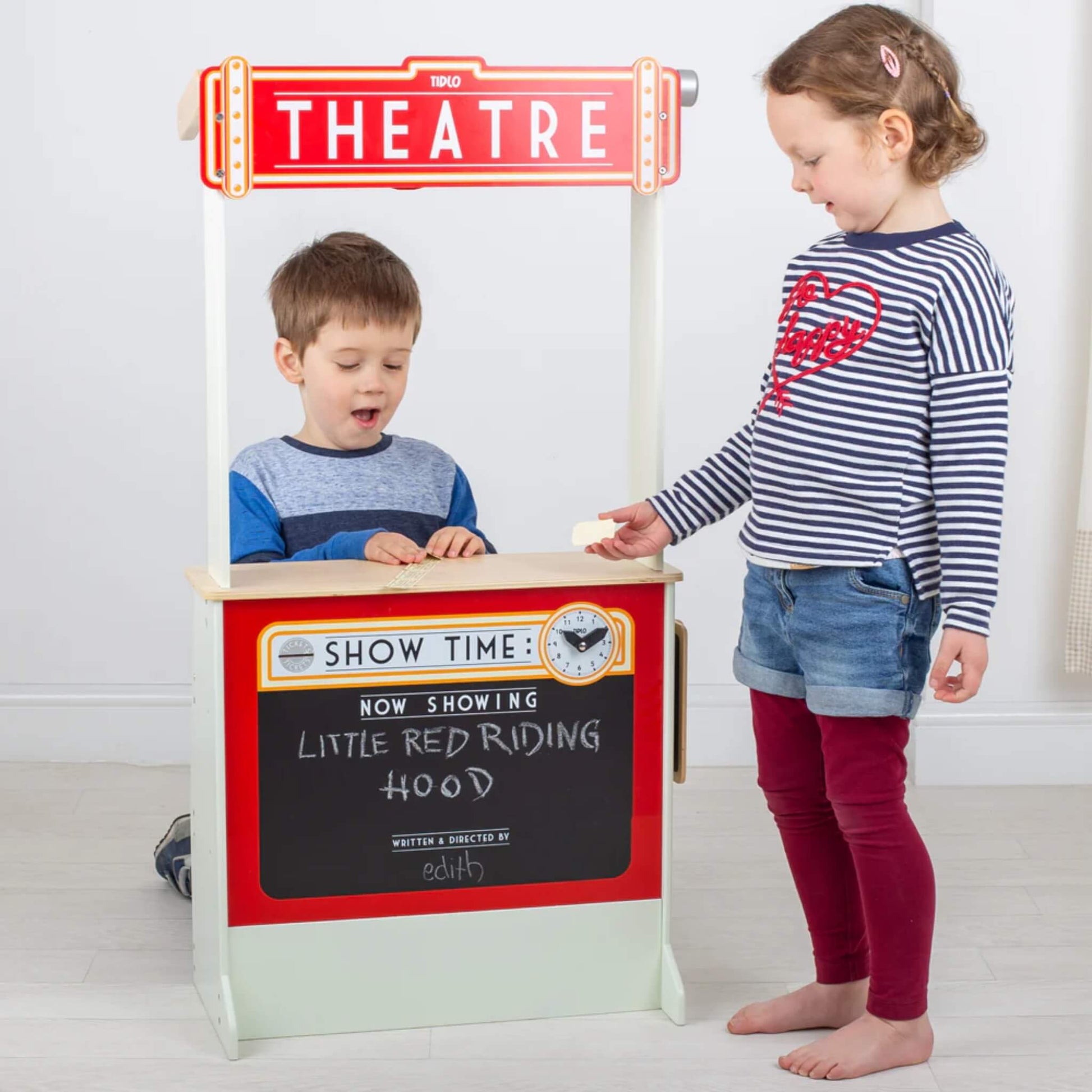 Child behind the theatre stand while another holds a ticket, both children actively engaged in storytelling and play.