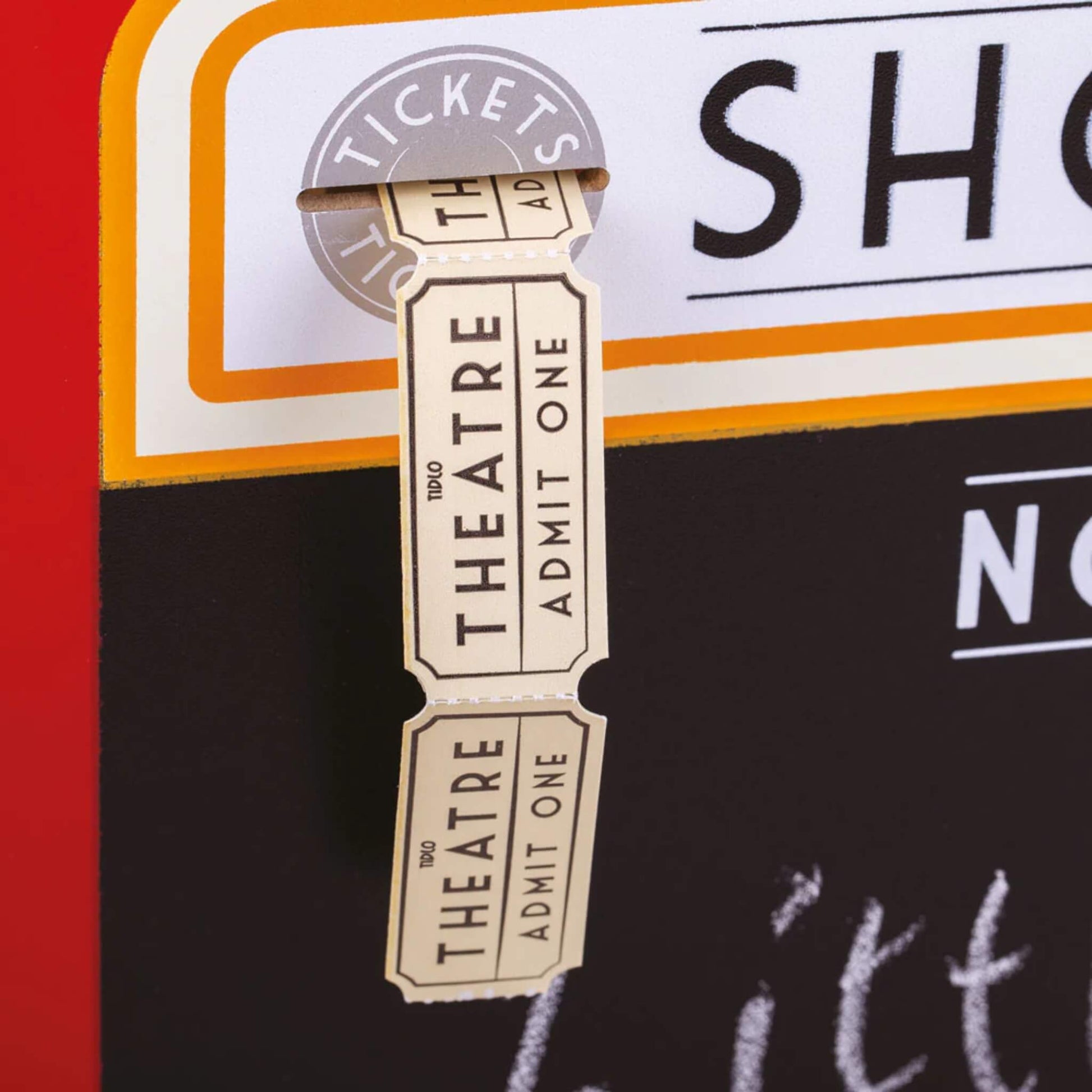 Close-up of the pretend theatre ticket reel labelled ‘Admit One’ being pulled from the dispenser on the front panel.