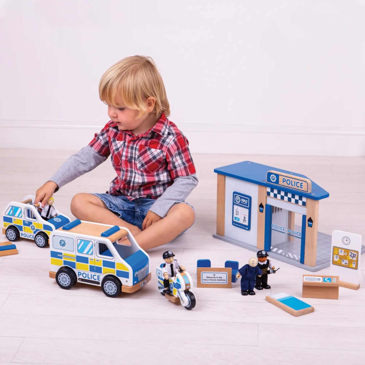 Young child playing on the floor with the full Tidlo police play set, including police vehicles, station, and the officer and prisoner figures in action.