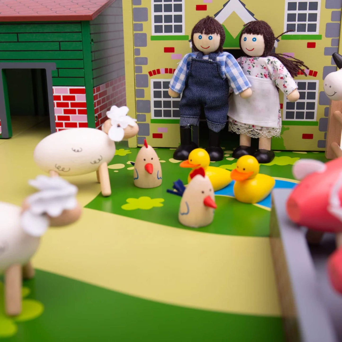 Two wooden farmer figures standing outside the farmhouse at Tidlo Oldfield Farm, surrounded by chickens, ducks and sheep in a colourful play scene.