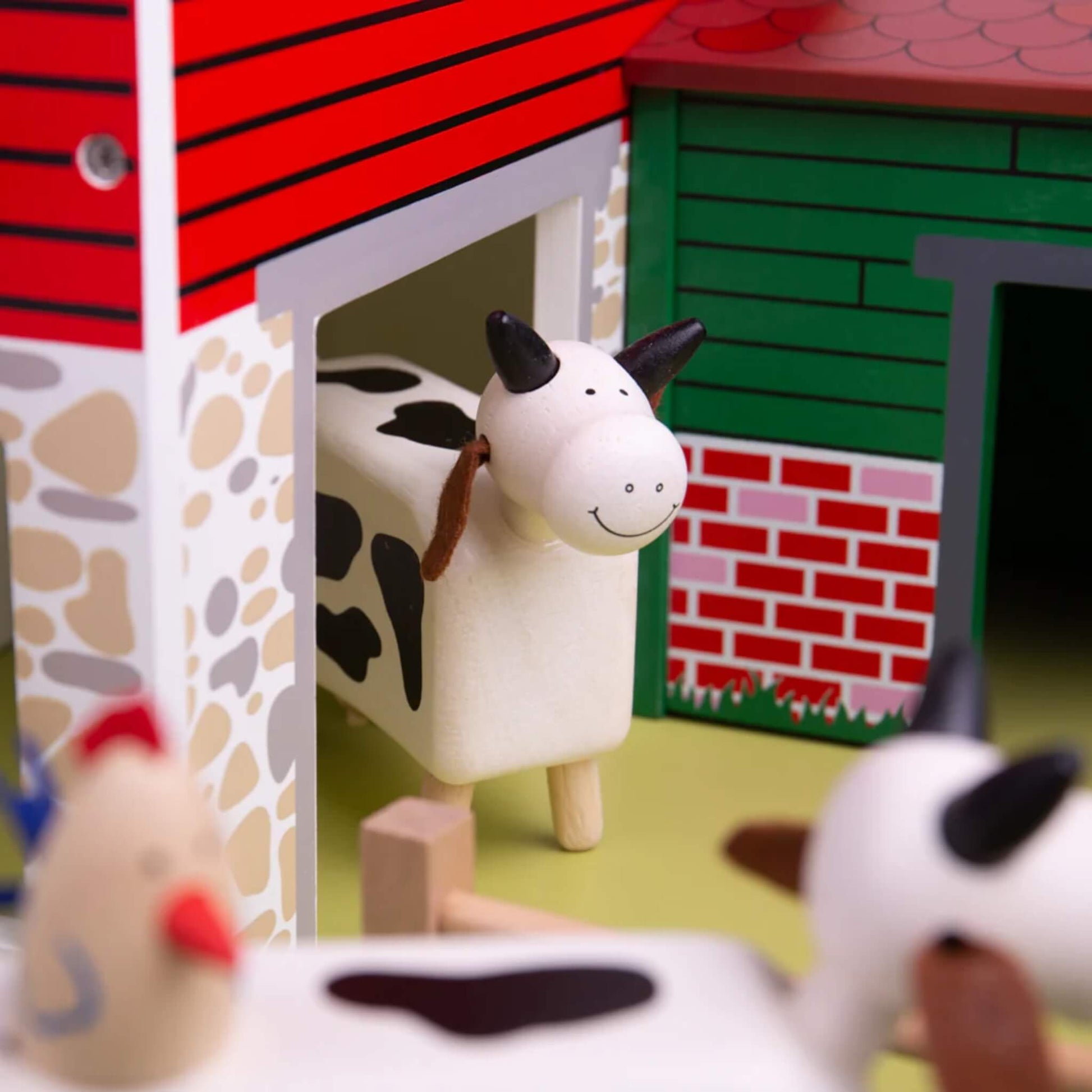 Black and white cow peeking out from the barn door of Tidlo Oldfield Farm, with chickens in the foreground and animal shed visible behind.