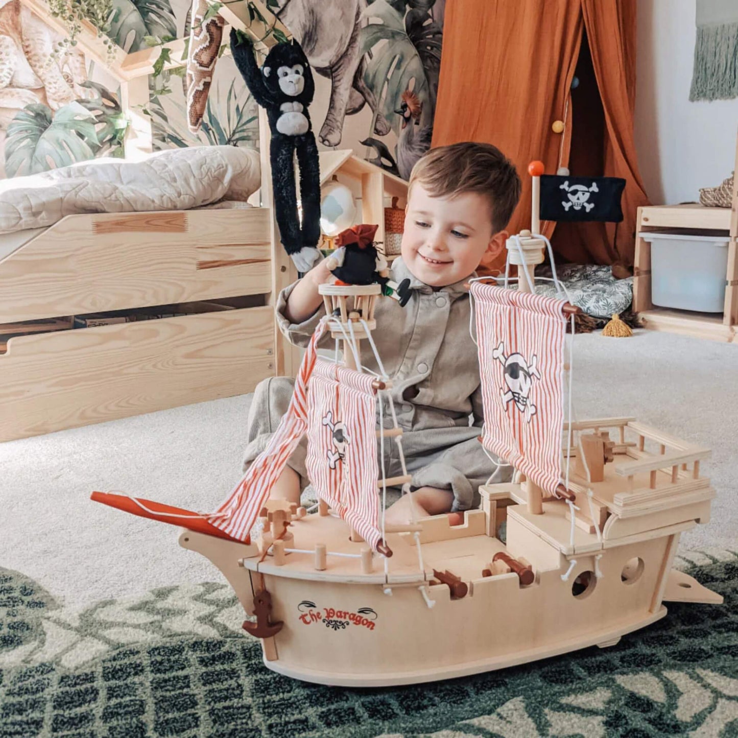 Child playing with the assembled Tidlo pirate ship in a jungle-themed bedroom, placing a pirate figure in the lookout post.