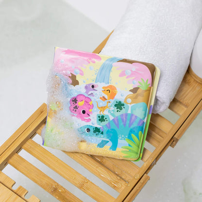 Tiger Tribe Messy Dinosaurs Bath Book resting on a wooden bath tray with bubbles, partially covered in foam and showing playful dinosaur illustrations.
