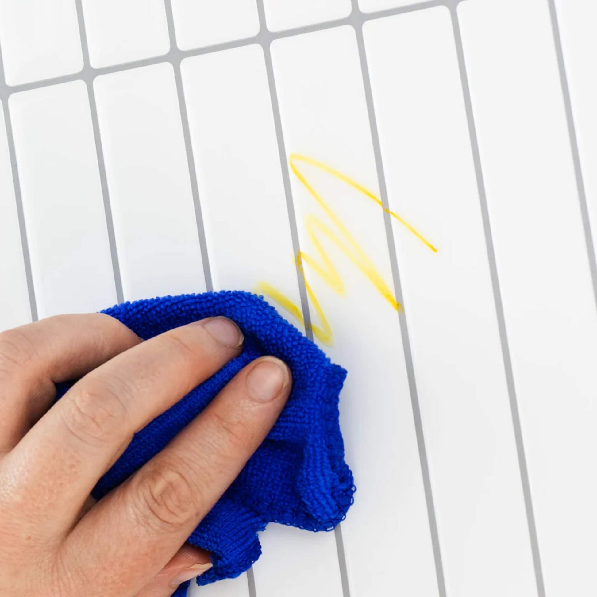 The same yellow crayon mark being wiped clean with a blue cloth on the tiled surface.
