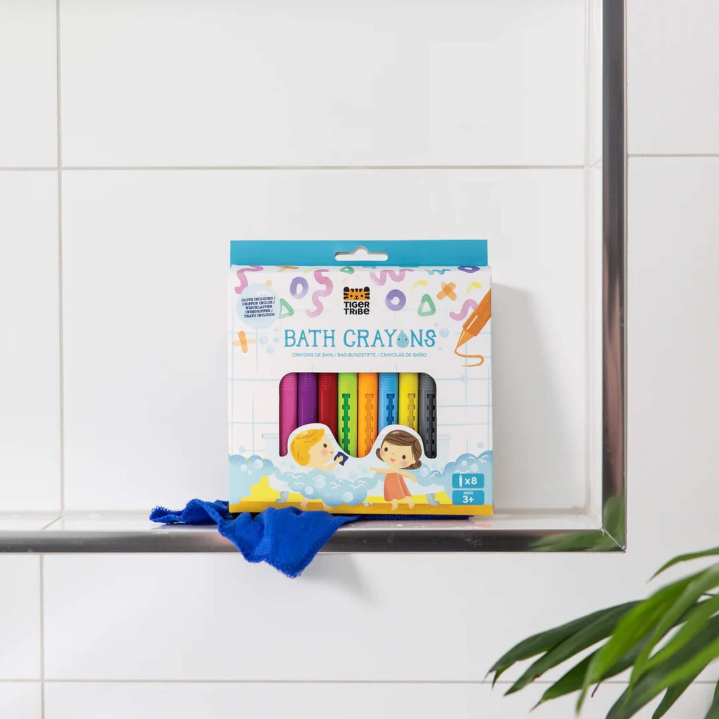 Tiger Tribe Bath Crayons box displayed upright on a tiled bathroom shelf, with the blue cloth resting underneath.