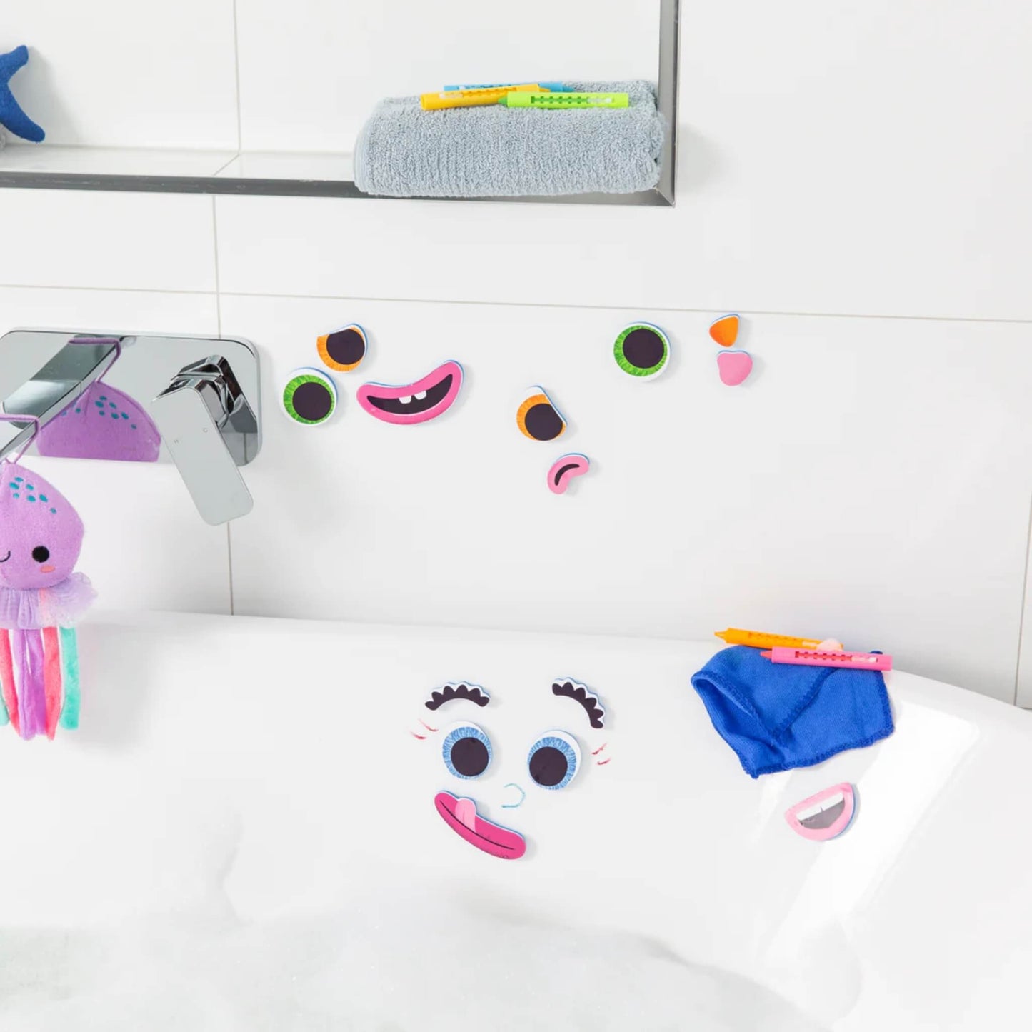 Multiple foam face pieces stuck to wet bath tiles, with more stored on the edge of the tub alongside bath crayons and cloth.