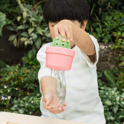 A child playing outdoors with the cactus toy, watching water stream from the base into their hand.