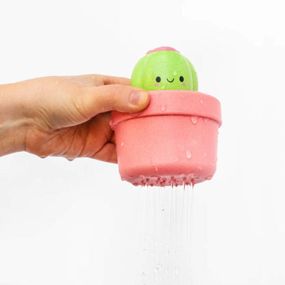 A hand holding the cactus toy over a white surface as water pours from the base holes.