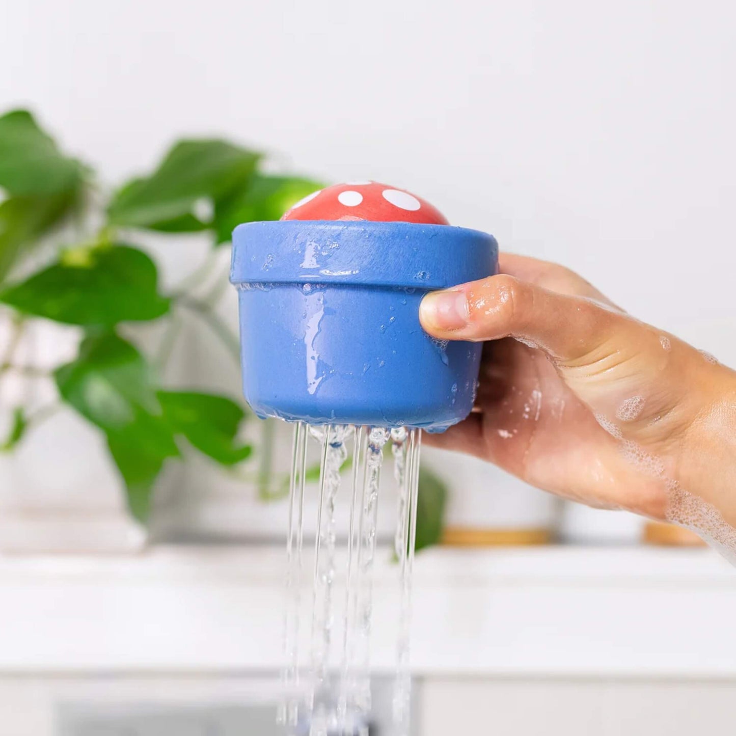 Child’s hand holding the toy over a sink, with water pouring through drainage holes.