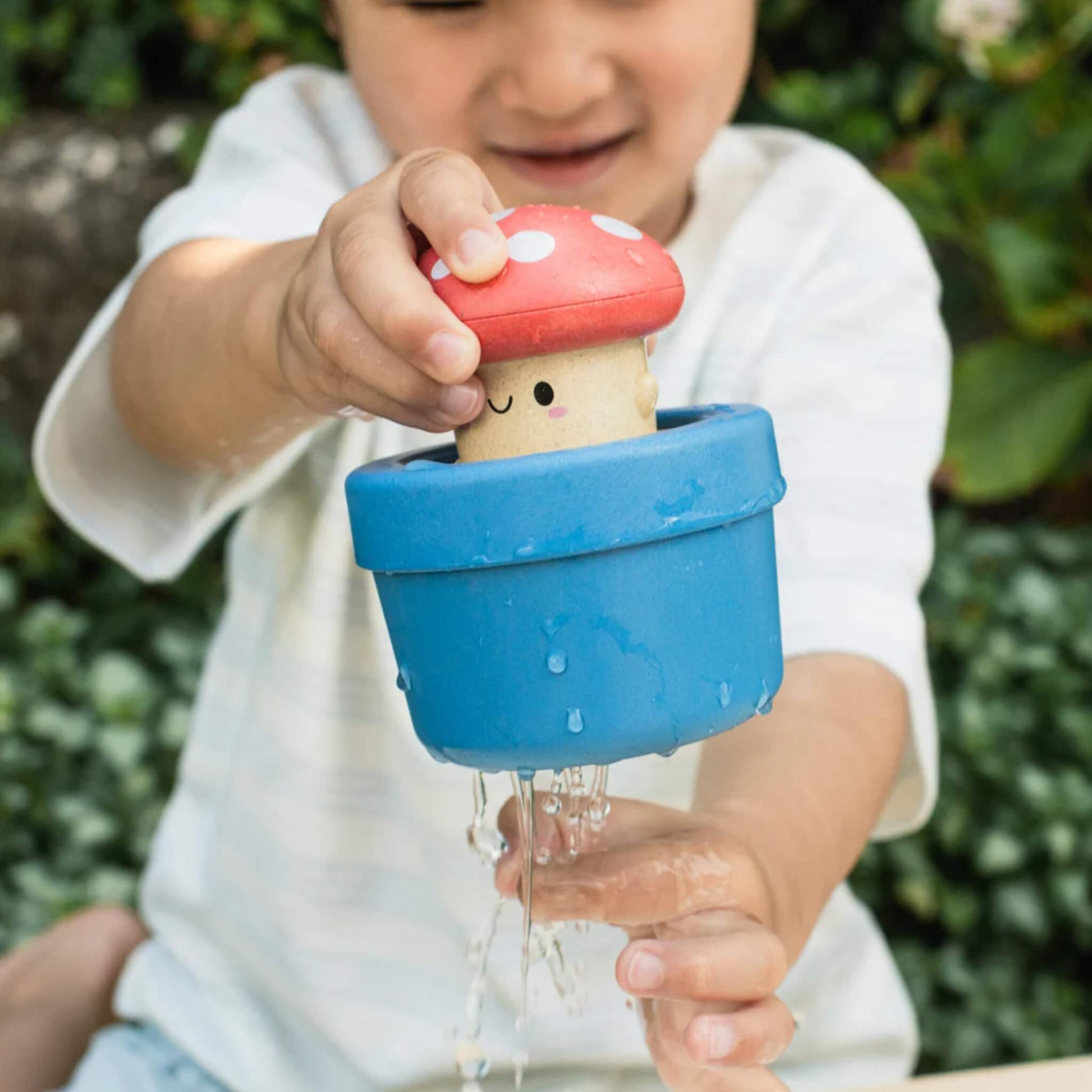 Toddler outdoors pushing the character down into the blue pot while water drips out.