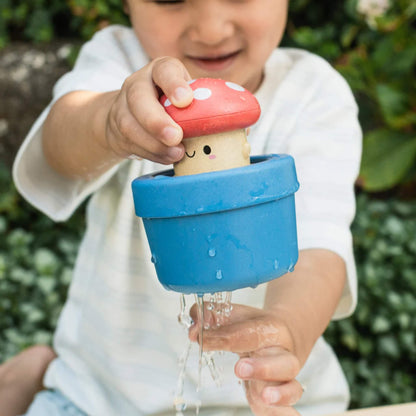 Toddler outdoors pushing the character down into the blue pot while water drips out.