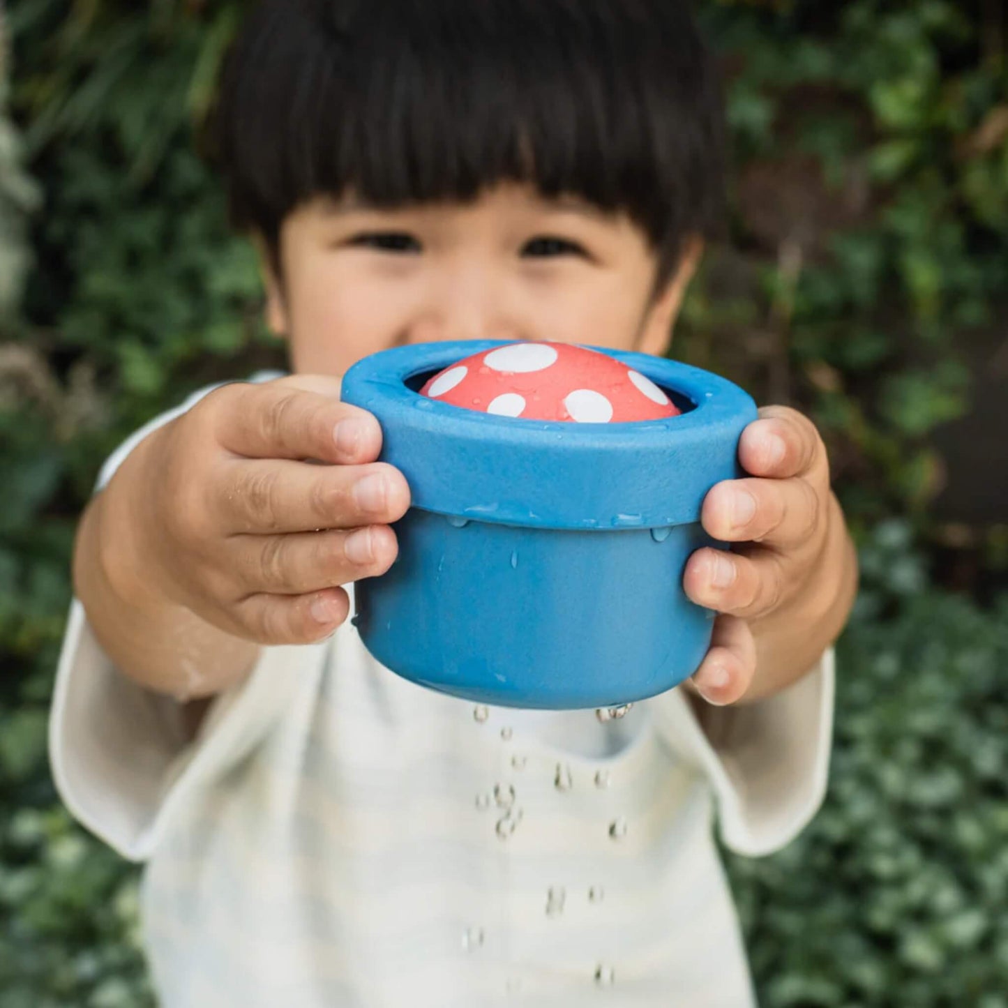 Child holding the bath toy in both hands as water trickles from the base.