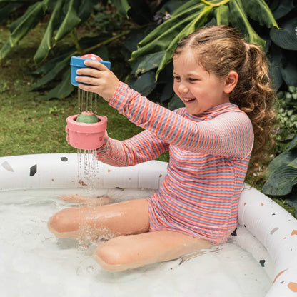 Young girl playing with two bath toys in a garden paddling pool, both draining water.