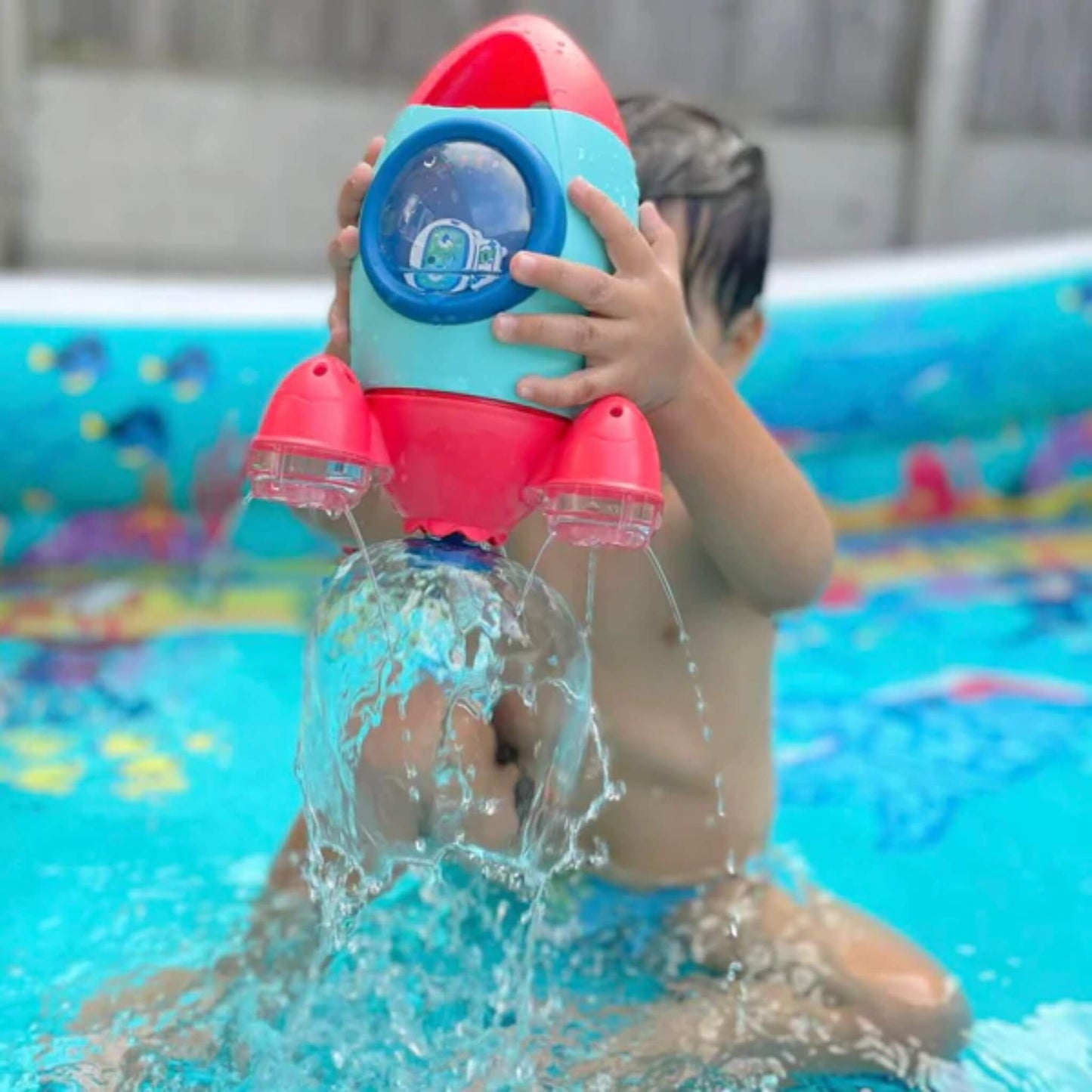 A child in a paddling pool holding the rocket high as water pours down in a dome shape from the spinning base.