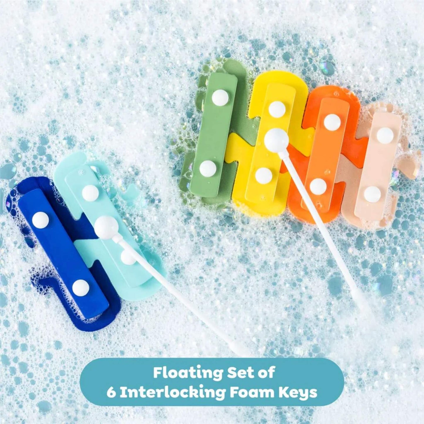 Foam xylophone keys floating in soapy bath water, interlocked in rainbow order with white mallets resting on top.