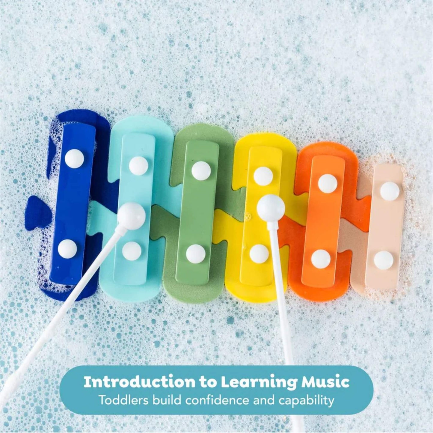 Close-up of the foam keys arranged in bath bubbles with two white mallets in use, demonstrating a musical learning activity.
