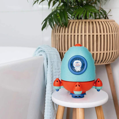 The ECO Bath Rocket displayed on a bathroom stool beside a tub, styled in a modern setting with a plant and textured towel.