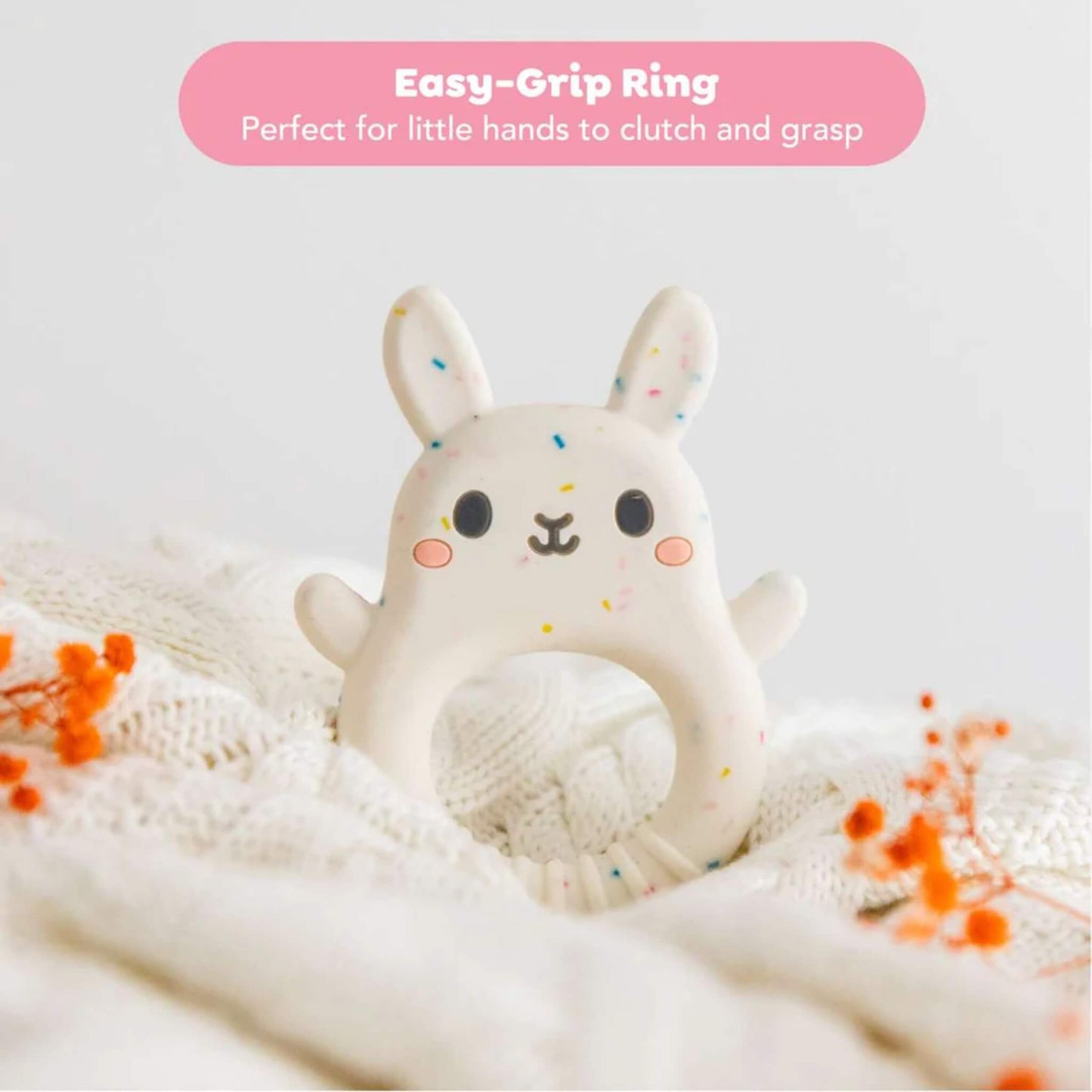 The bunny teether sits upright, surrounded by soft fabric and orange dried flowers, with a label reading ‘Easy-Grip Ring’.