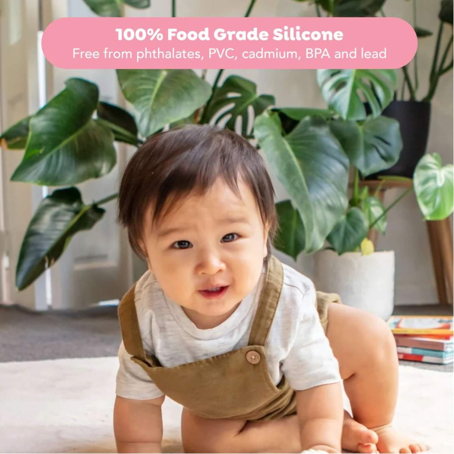 A baby in a beige romper looks up while playing indoors, with the caption ‘100% Food Grade Silicone’ overlaid.
