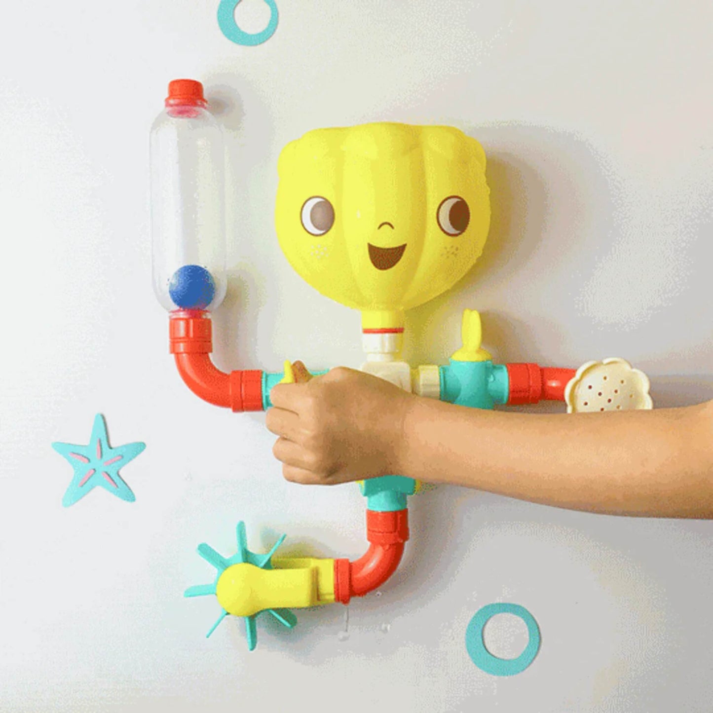 Child turning a valve on the wall-mounted bath toy, activating the water spinner and directing flow through colourful pipe pieces.