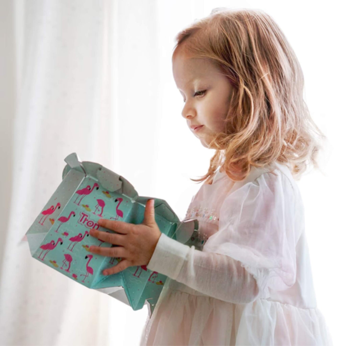Young child in a white dress holds the assembled flamingo-print disposable potty while standing indoors.