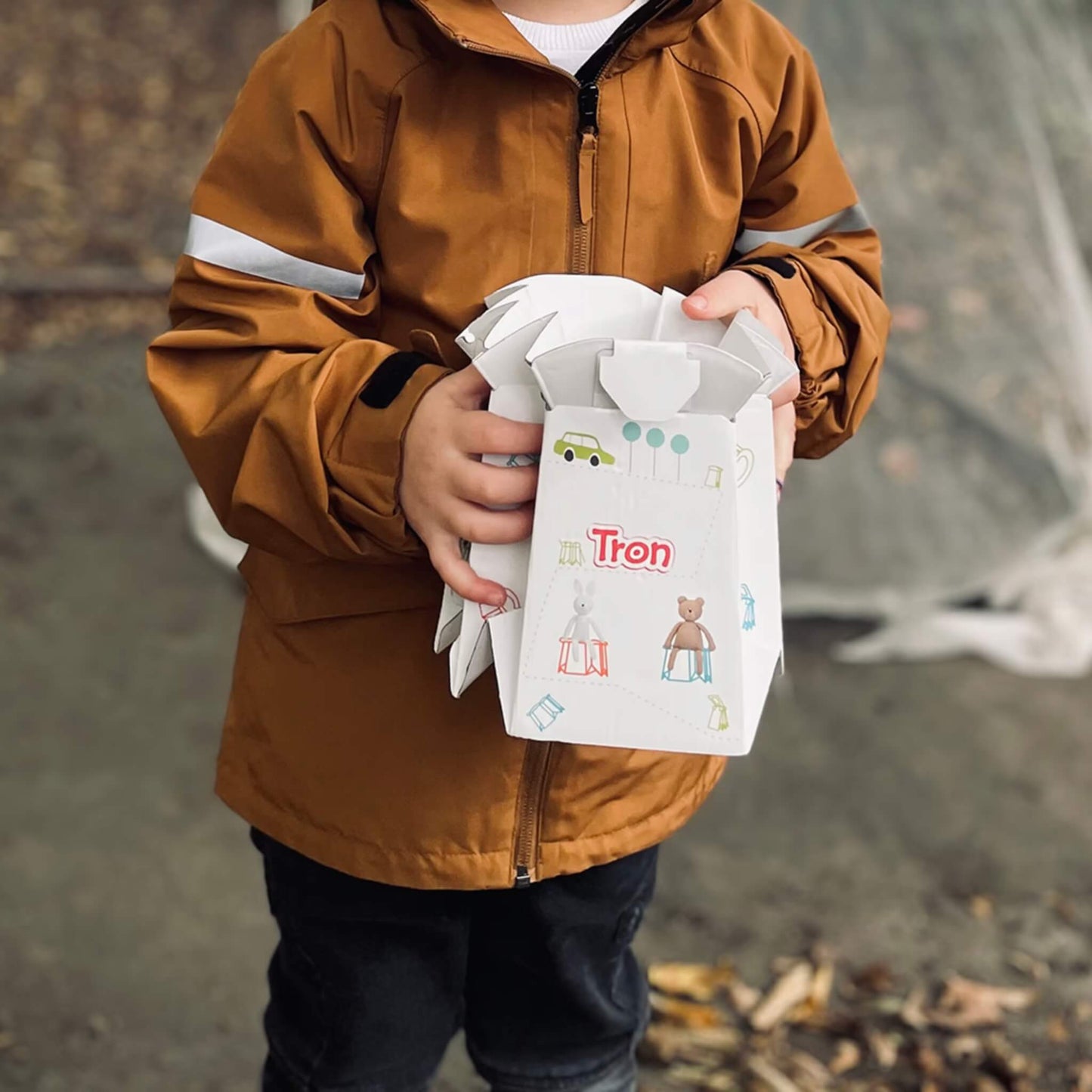 Child in a brown coat holding a folded disposable potty with rabbit and bear design.