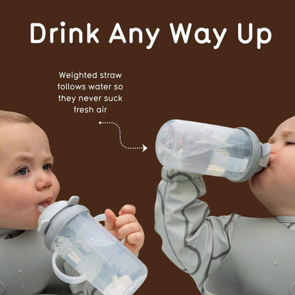 Two babies wearing gray bibs are shown drinking from translucent sippy cups with weighted straws against a dark brown background with marketing text.