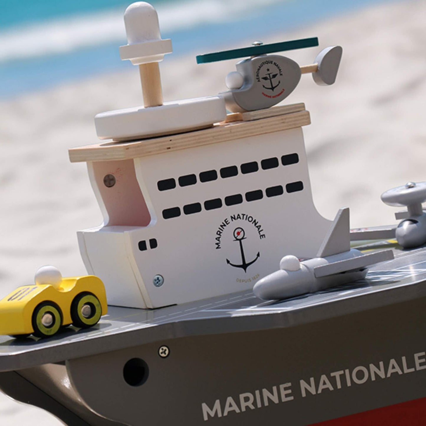 A close-up of the superstructure of a wooden aircraft carrier showing a helicopter on top and a yellow deck vehicle beside it.