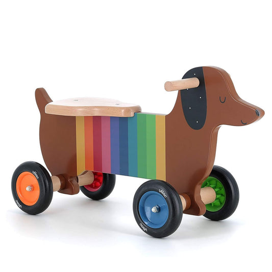 Vilac Andy Westface Dog Ride On wooden toy with rainbow striped body, dachshund shape, wooden seat and multicoloured wheels.