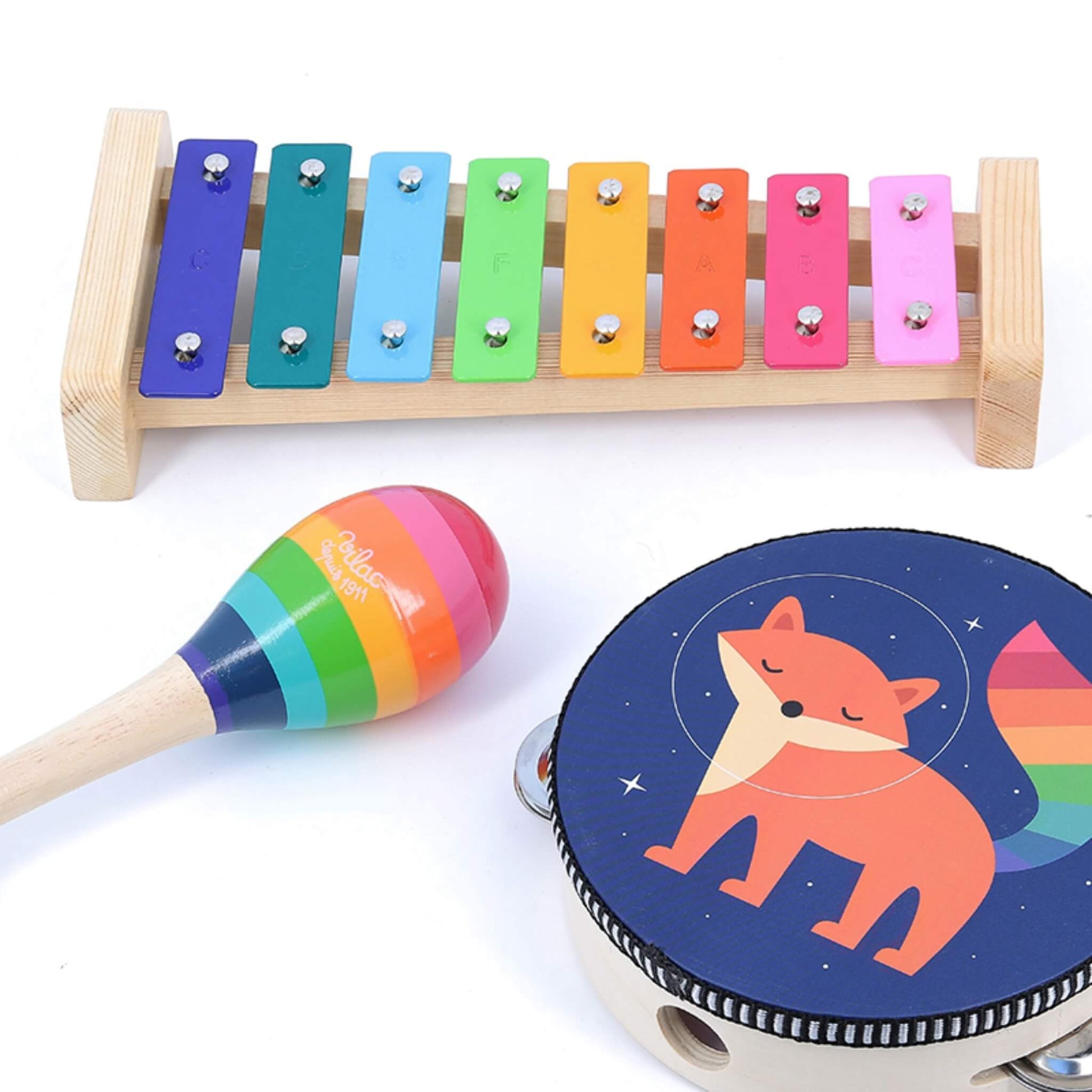 A rainbow-coloured xylophone with a wooden frame, a striped maraca, and a tambourine decorated with a fox illustration.