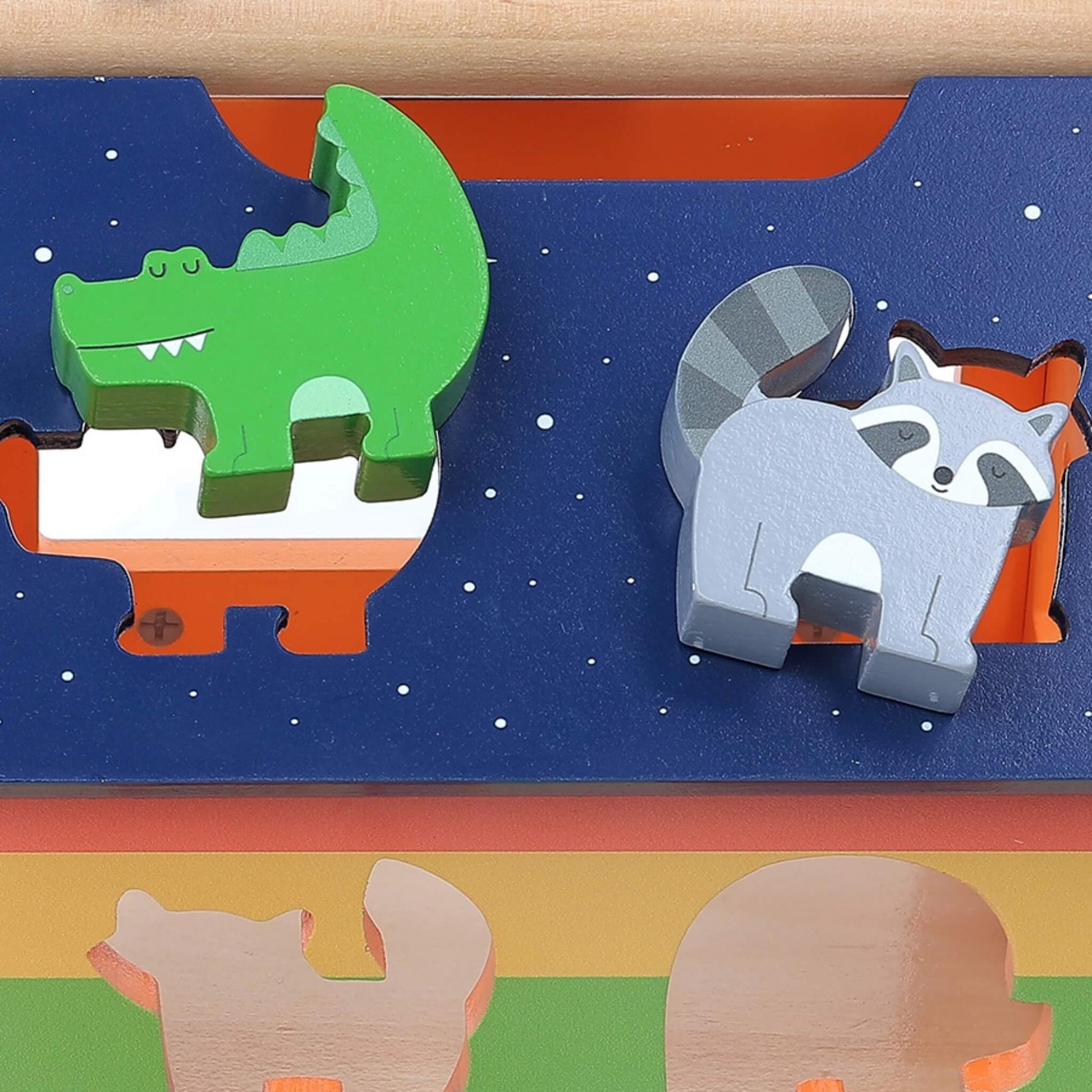 Close-up of a green crocodile and grey raccoon wooden block fitted into starry blue roof slots of a shape sorter.