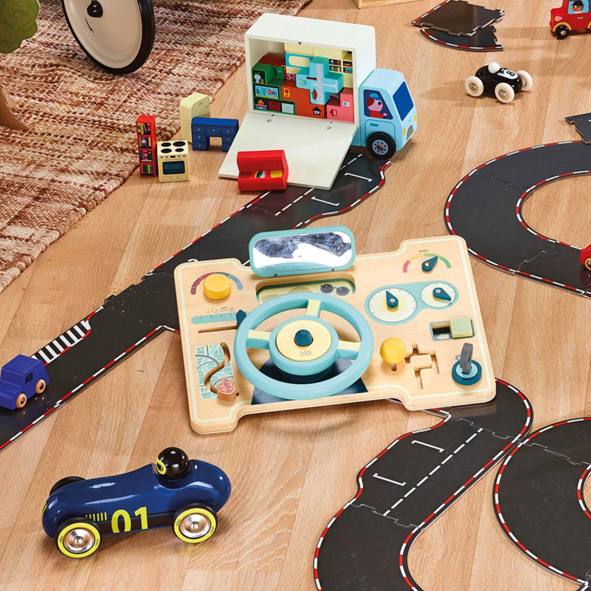 Wooden car activity board placed on playroom floor with toy road set and vehicles, showing realistic driving layout and interactive features.