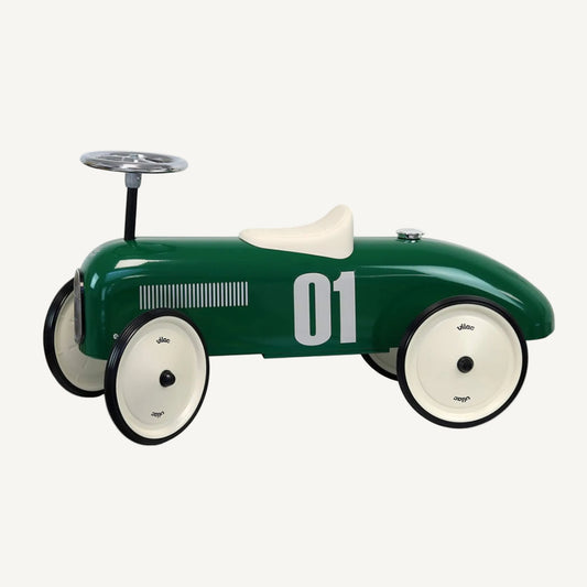 Vintage style ride-on toy car in dark green with cream seat, black wheels and chrome steering wheel viewed from side profile.