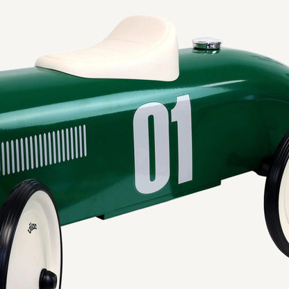 A close-up of the front section of a green ride-on toy car showing a chrome grille, front wheel, steering column and part of the bonnet.