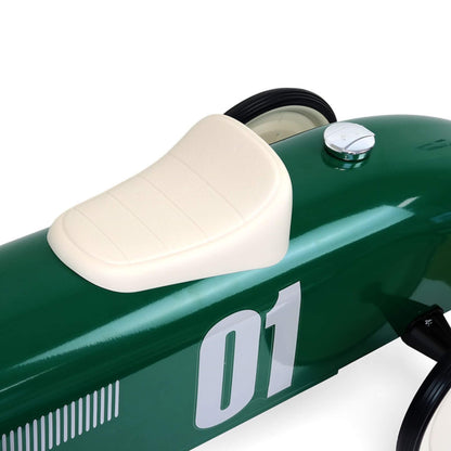 A close-up of a cream padded seat mounted on a glossy green metal body with a silver fuel cap positioned behind the seat.