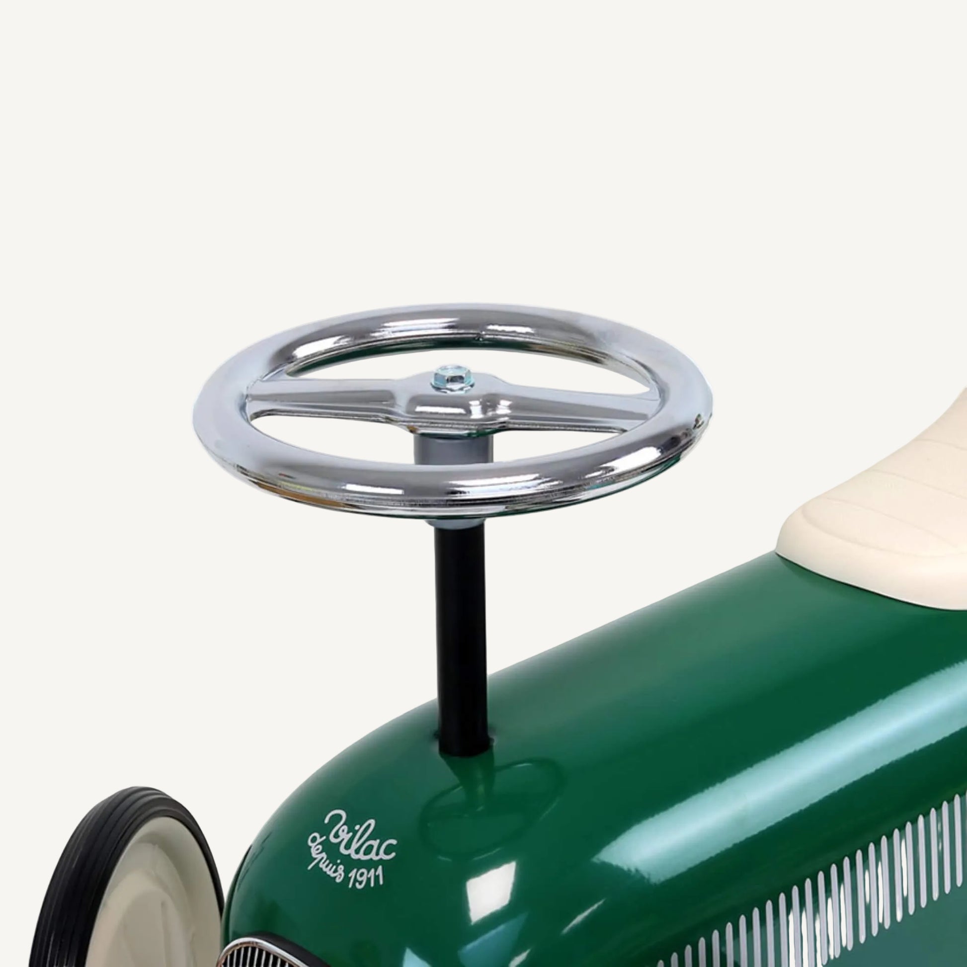 A close-up of a round chrome steering wheel attached to a black vertical column on top of a green metal ride-on toy car.